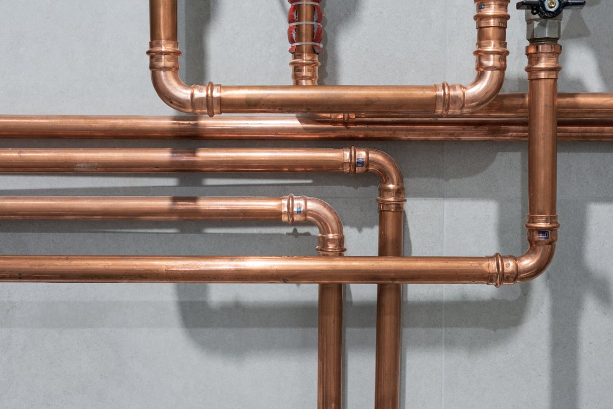 Copper pipes joined with pressed fittings against a grey tiled wall